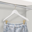 White hanger with gold clips holding a pair of blue patterned pants on a white rack.