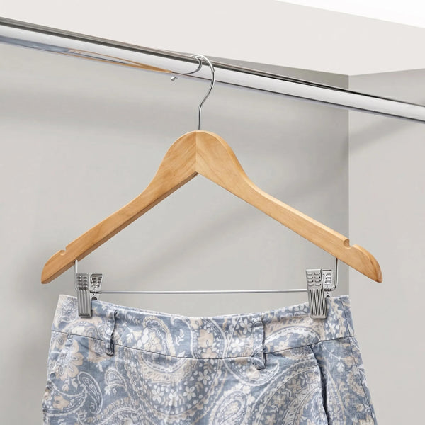 Wooden hanger with a pair of pants on a metal rod against a gray wall.