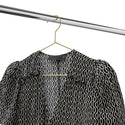Black and white patterned blouse hanging on a gold metal coat hanger on a chrome clothes rack