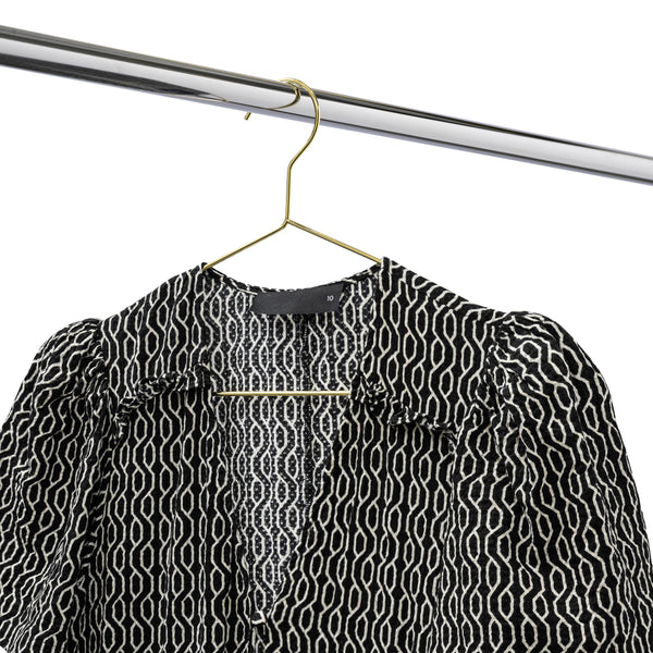 Black and white patterned blouse hanging on a gold metal coat hanger on a chrome clothes rack