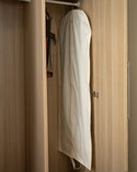 A beige colour cotton garment bag hanging on a metal clothes rail inside a wardrobe