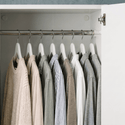Clothing items on hangers inside a wardrobe with neutral colors.