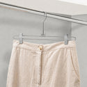 Beige pants hanging on a metal hanger against a neutral background