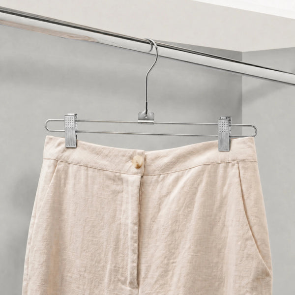 Beige pants hanging on a metal hanger against a neutral background