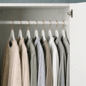 Clothing items on hangers inside a wardrobe with neutral colors.