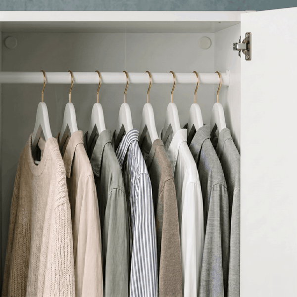Clothing items on hangers inside a wardrobe with neutral colors.