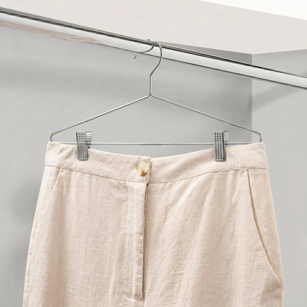 Beige pants on a metal hanger against a neutral background