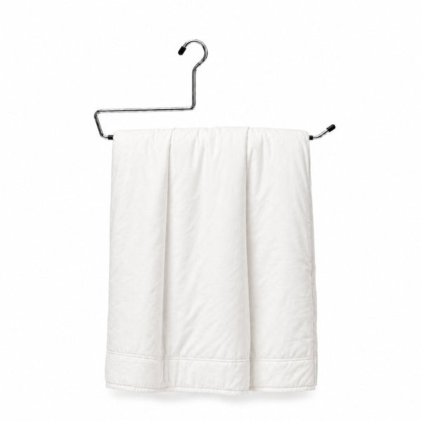 Metal hanger holding a folded white duvet cover on a plain background