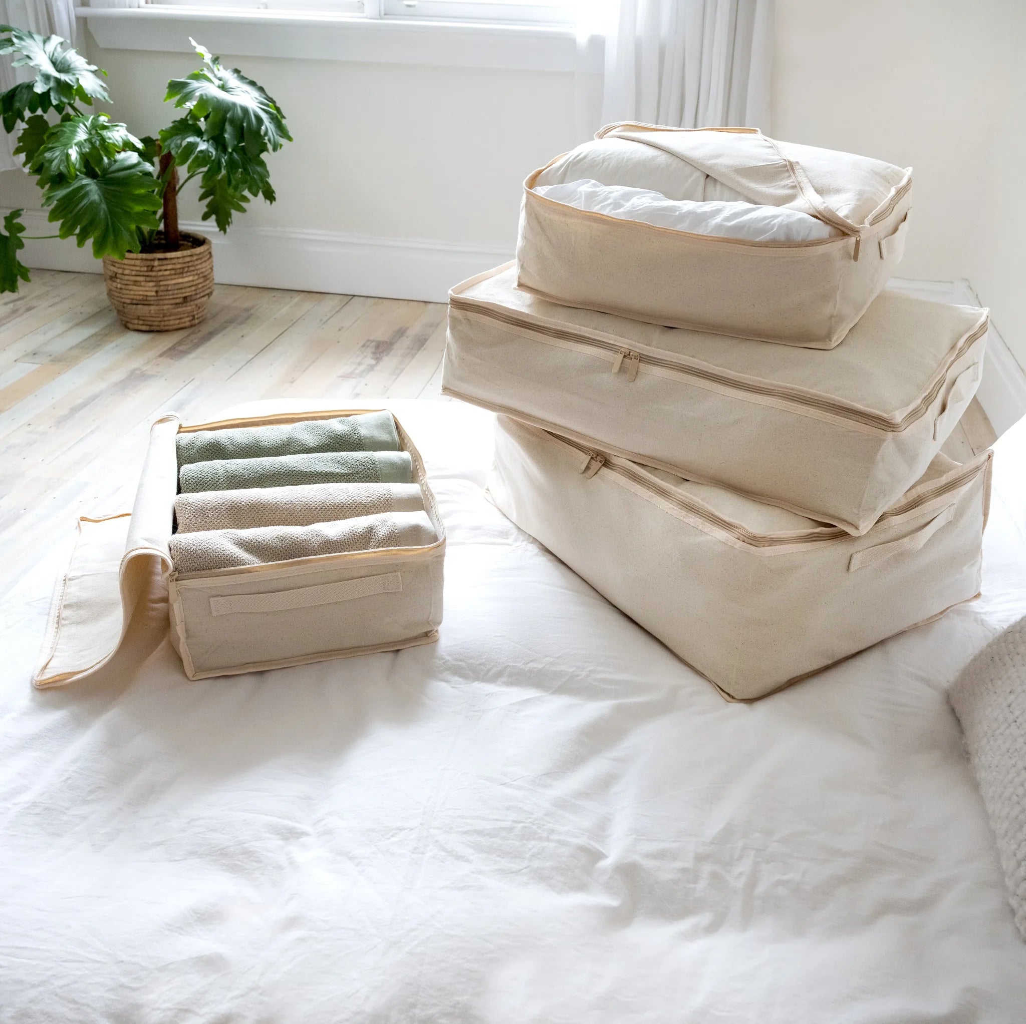 Set of beige storage bags on a bed with a plant in the background