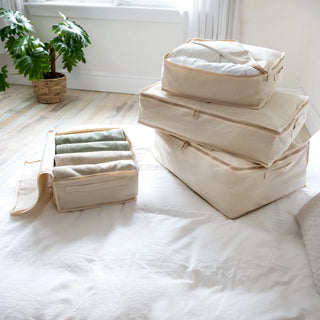 Set of beige storage bags on a bed with a plant in the background